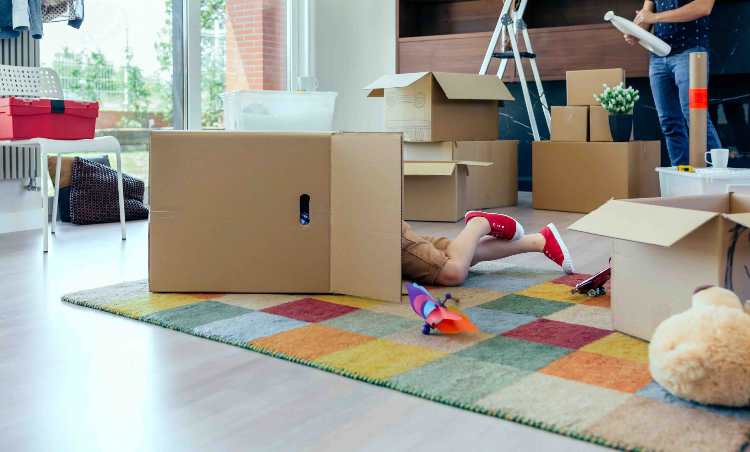 Little boy playing inside a moving box while his father unpacks in the living room